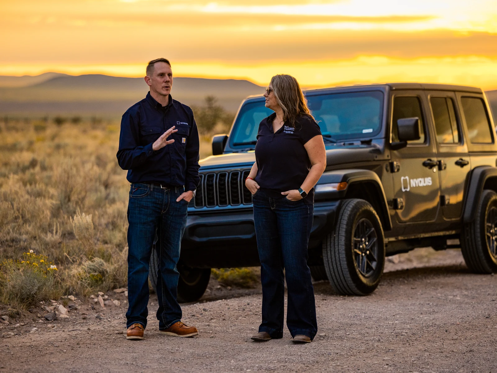 Two people beside a Nyquis-branded vehicle at sunset.