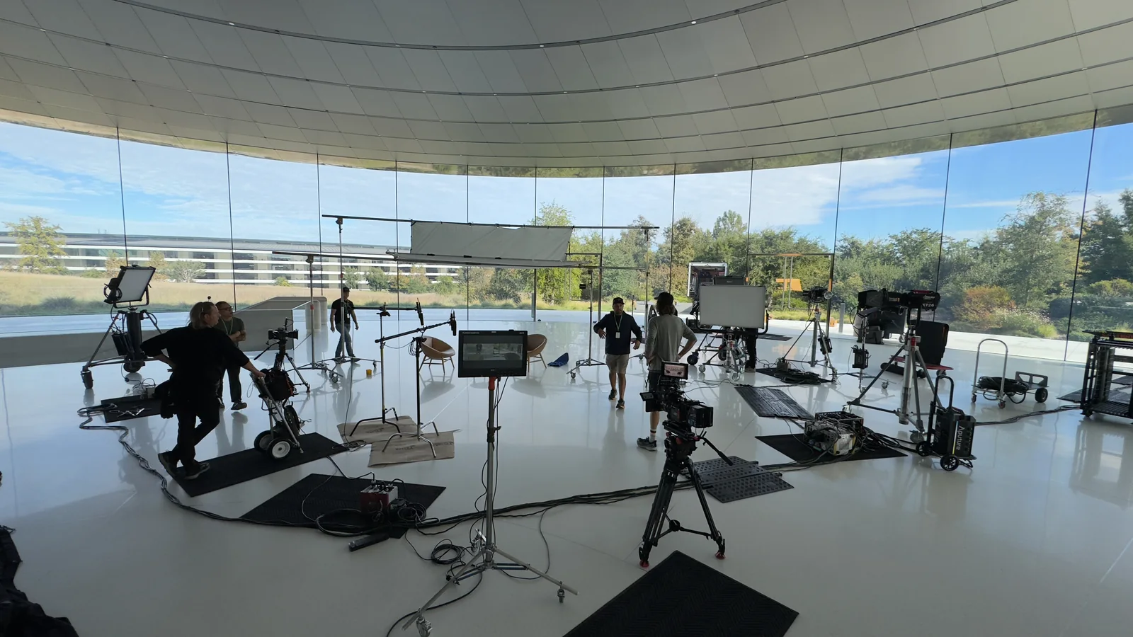 A wide production setup with cameras and lighting in a glass-walled space.