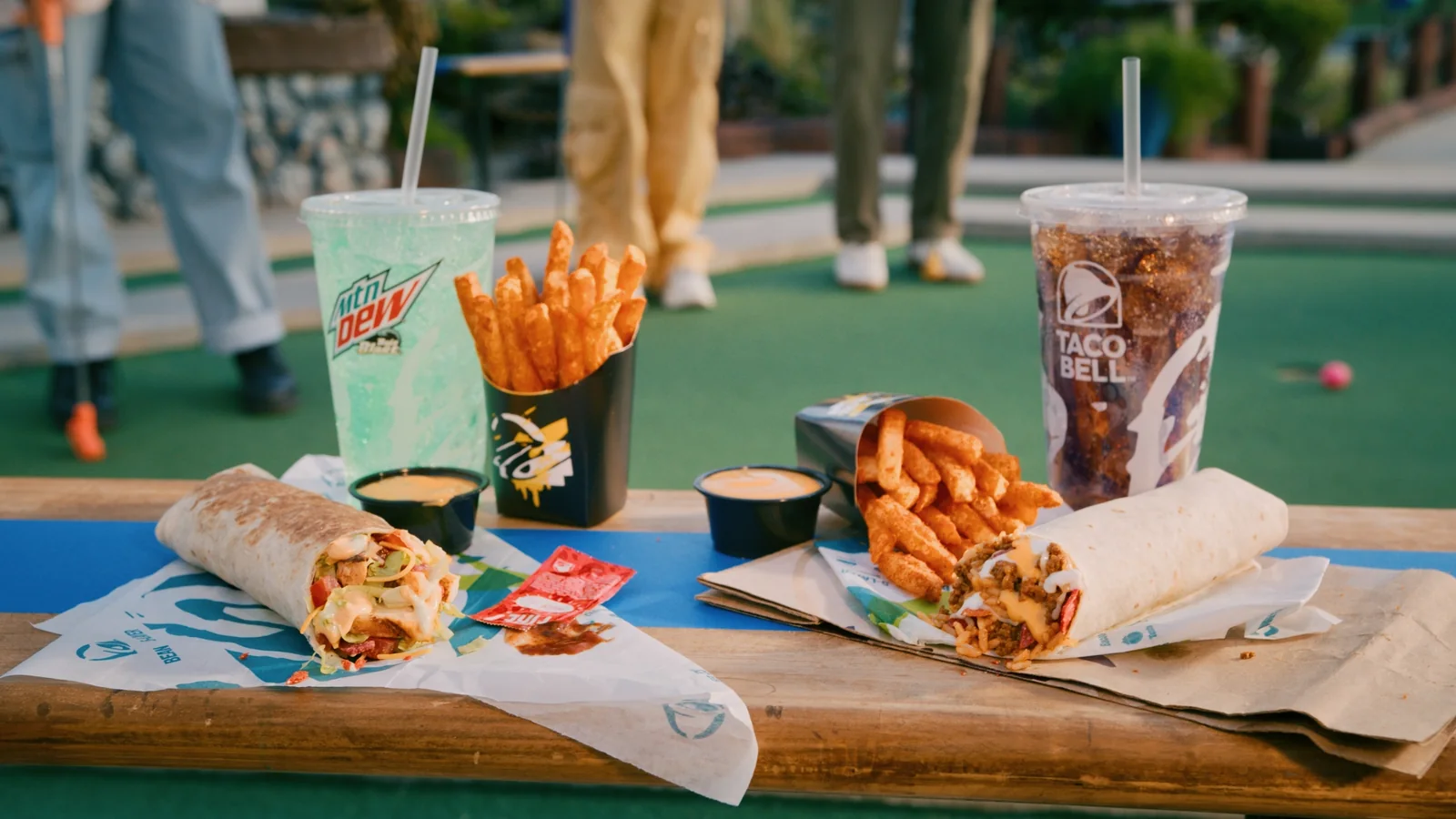Taco Bell food and drinks on an outdoor table in a campaign frame.