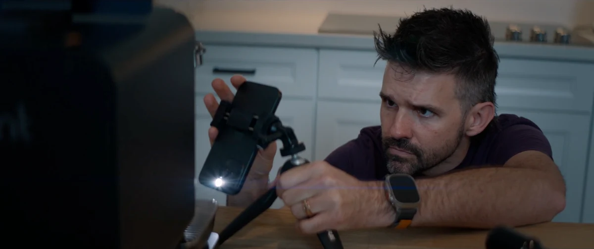 A man positions an iPhone on a small tripod beside his coffee setup.