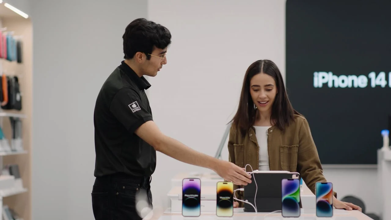 A sales associate showing a customer Apple products at a retail display.